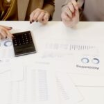 Two professionals analyzing financial documents with a calculator.
