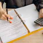 A woman reviewing documents and using a calculator on a wooden table.