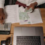 Close-up of a person counting cash with documents and a laptop in an office setting.